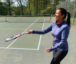 Kvinna på tennisbana, i bakgrunden gröna träd. 