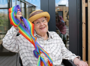 Äldre dam håller regnbågsfärgat band i handen
