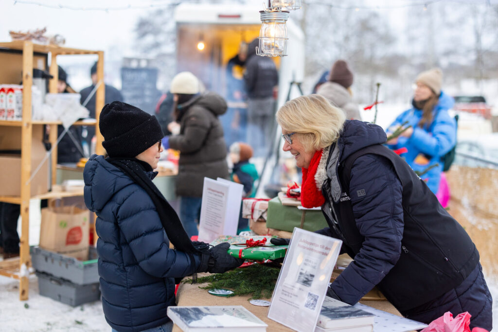 Barn lämnar ett paket till kvinna vid bort fyllt av julklappar.