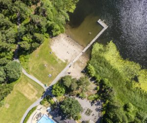 Grönt strandområde, sandstrand och brygga som går ut i sjö