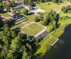 Vy över grönt parkområde och en u-formad brygga ut i sjö. 
