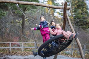 Tre barn i galonisar gungar på stor gunga utomhus på den fina gården på förskolan Borgen i Sköndal.