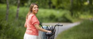 Leende kvinna som leder cykel längs lummig cykelväg.