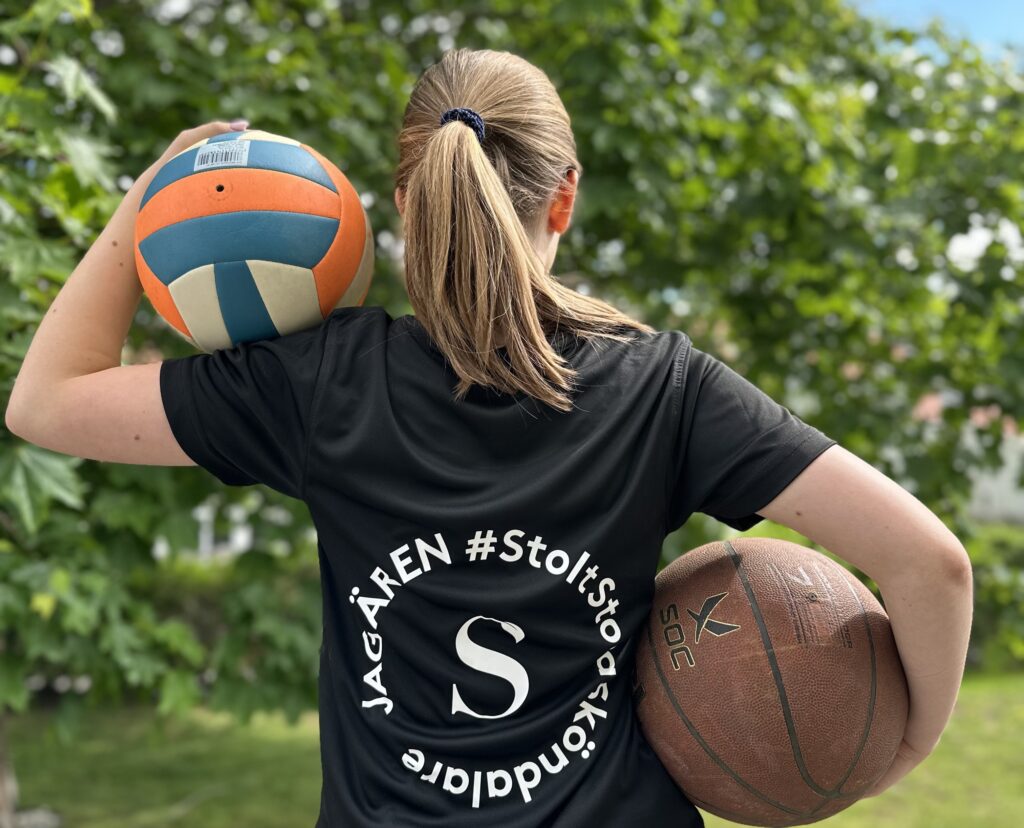 Ryggen på en tjej som håller en volleyboll och en fotboll. På tröjan står "Stolt Stora Sköndalare"